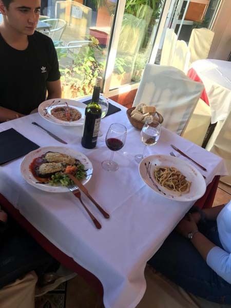 Un hombre se sienta a una mesa con platos de comida y una botella de vino.