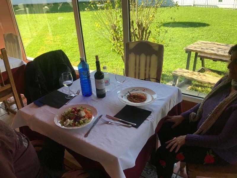 Una mujer está sentada en una mesa con platos de comida y una botella de vino.