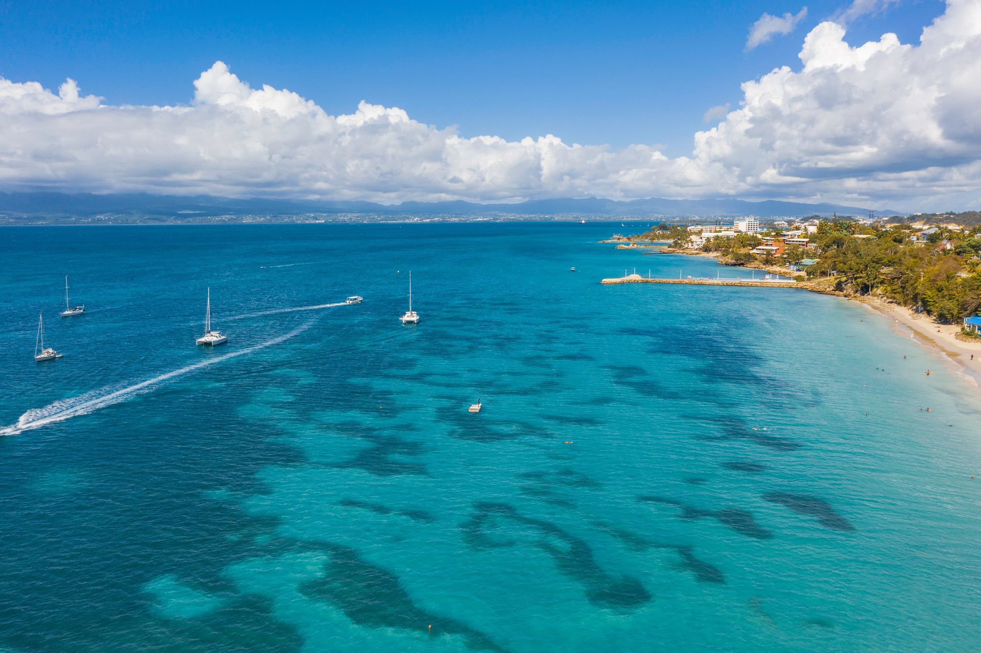 Baie turquoise avec des voiliers, plage de sable blanc et ciel bleu nuageux