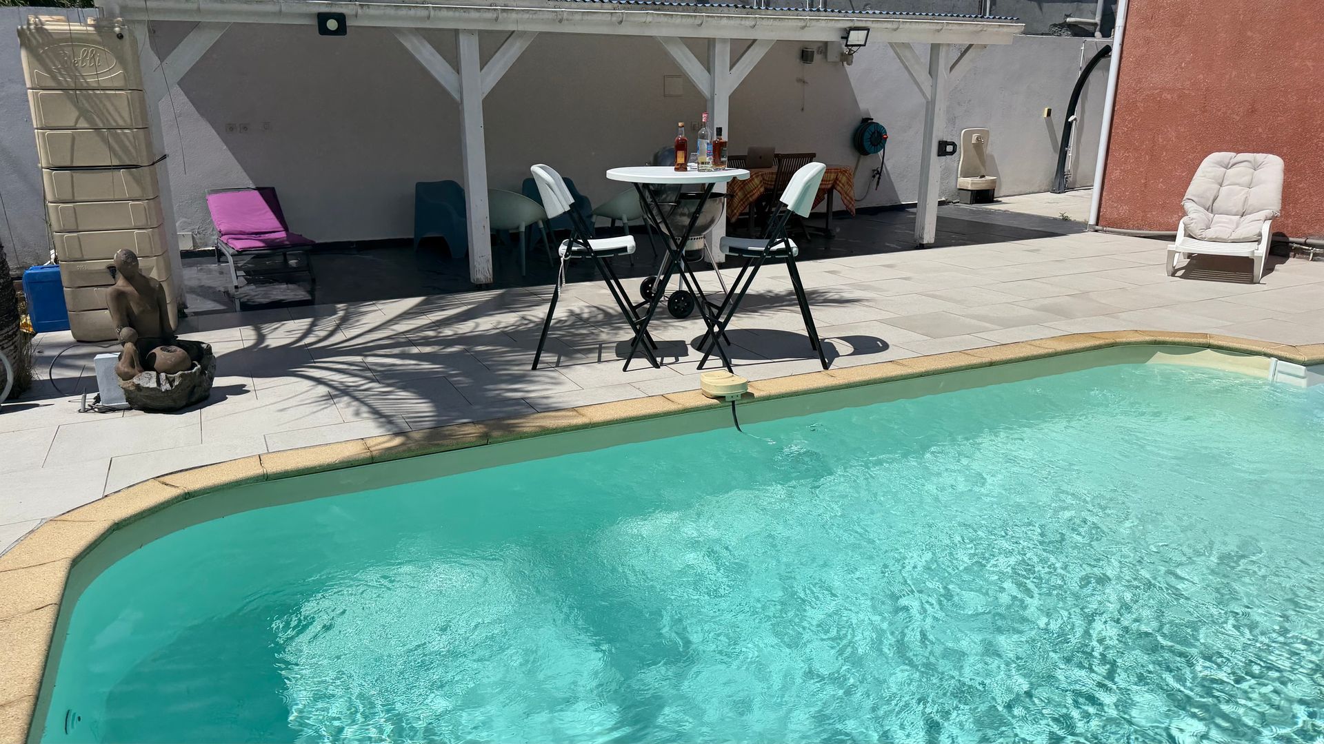 Piscine dans le jardin avec eau turquoise, mobilier de terrasse et coin salon ombragé près d'un mur