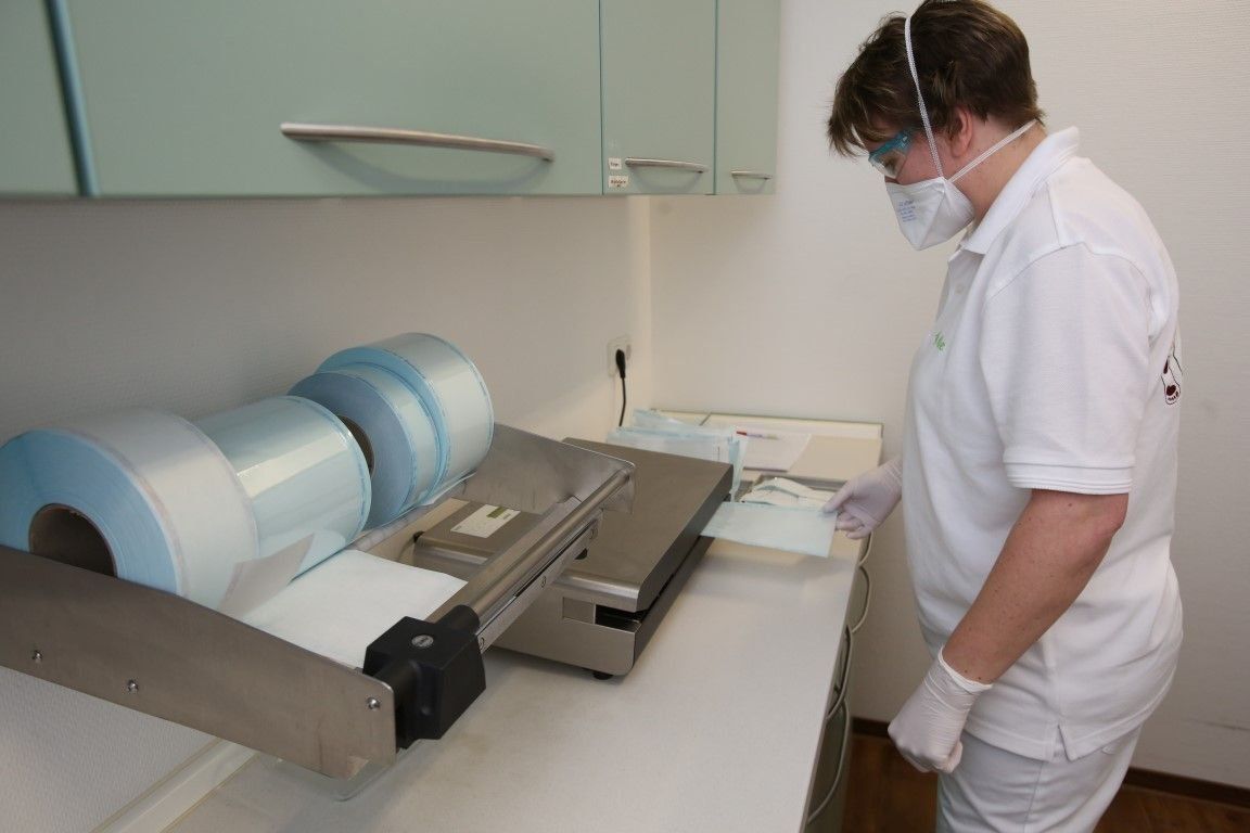 Eine Person in medizinischer Kleidung verwendet eine Versiegelungsmaschine für sterile Verpackungen in einer medizinischen Umgebung.