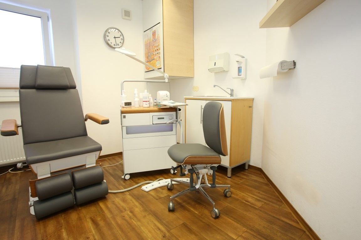 Podologenpraxis: Stuhl, Geräte und ein Behandlungsstuhl mit Fußstützen auf einem Holzboden.