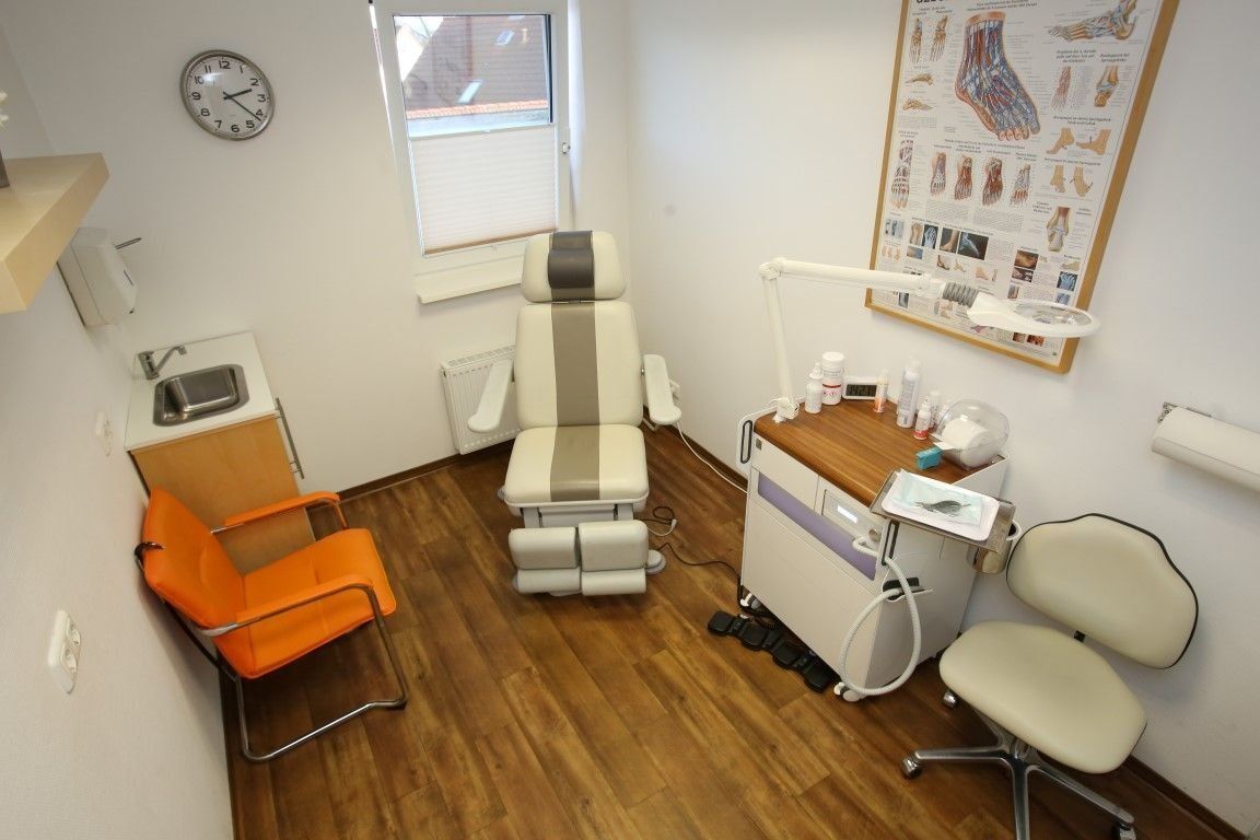 Podologenpraxis mit Behandlungsstuhl, Waschbecken, orangefarbenem Stuhl und medizinischer Ausrüstung.