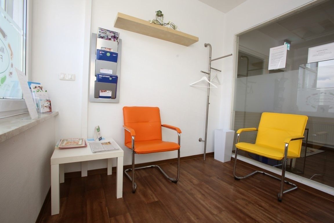 Ein Wartezimmer mit orangefarbenen und gelben Stühlen, einem weißen Tisch und einem Holzboden.