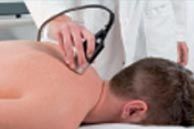 Terapeuta utilizando un dispositivo portátil en la parte superior de la espalda de un paciente durante el tratamiento.
