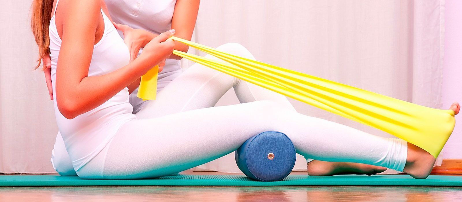 Persona haciendo ejercicio con una banda de resistencia amarilla sobre una esterilla de yoga, usando un rodillo de espuma para apoyarse.