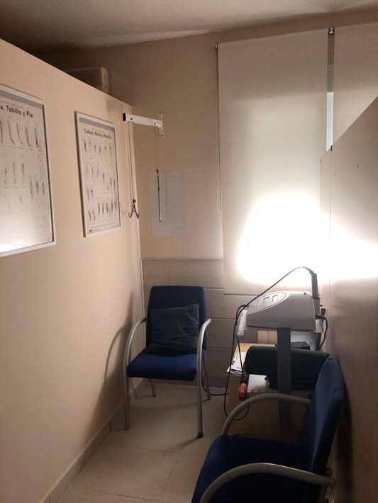 Pequeña oficina con dos sillas azules, un escritorio y luz solar brillante que entra por una ventana.