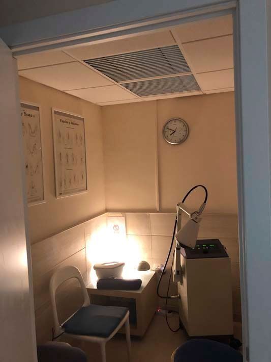 Habitación pequeña con poca luz, con una silla, una lámpara encendida, un reloj de pared y equipo médico.