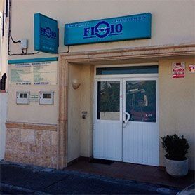Entrada a la tienda con un letrero azul sobre una puerta doble blanca, junto a una planta en maceta.