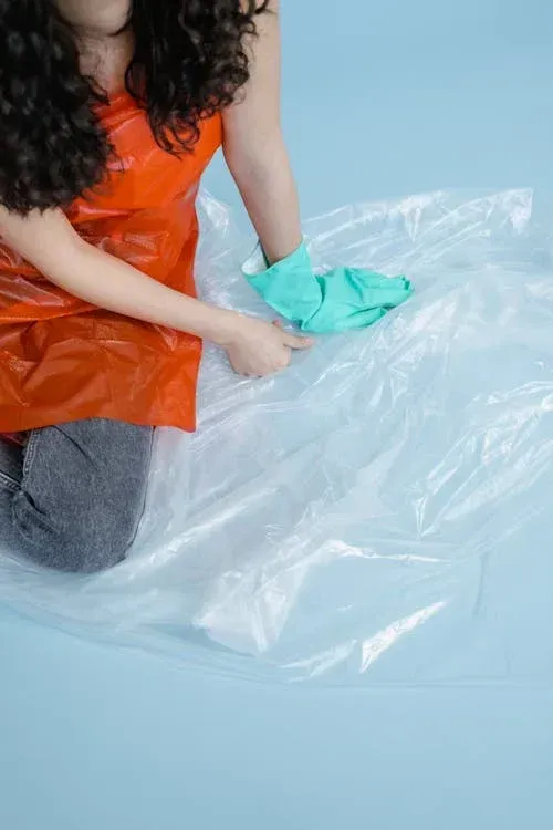 Uma mulher está ajoelhada sobre um saco plástico no chão.