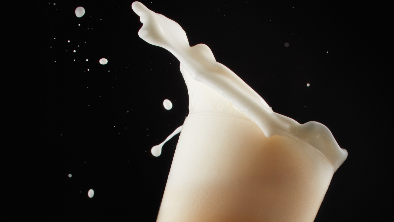 Leche salpicando de un vaso sobre un fondo negro.