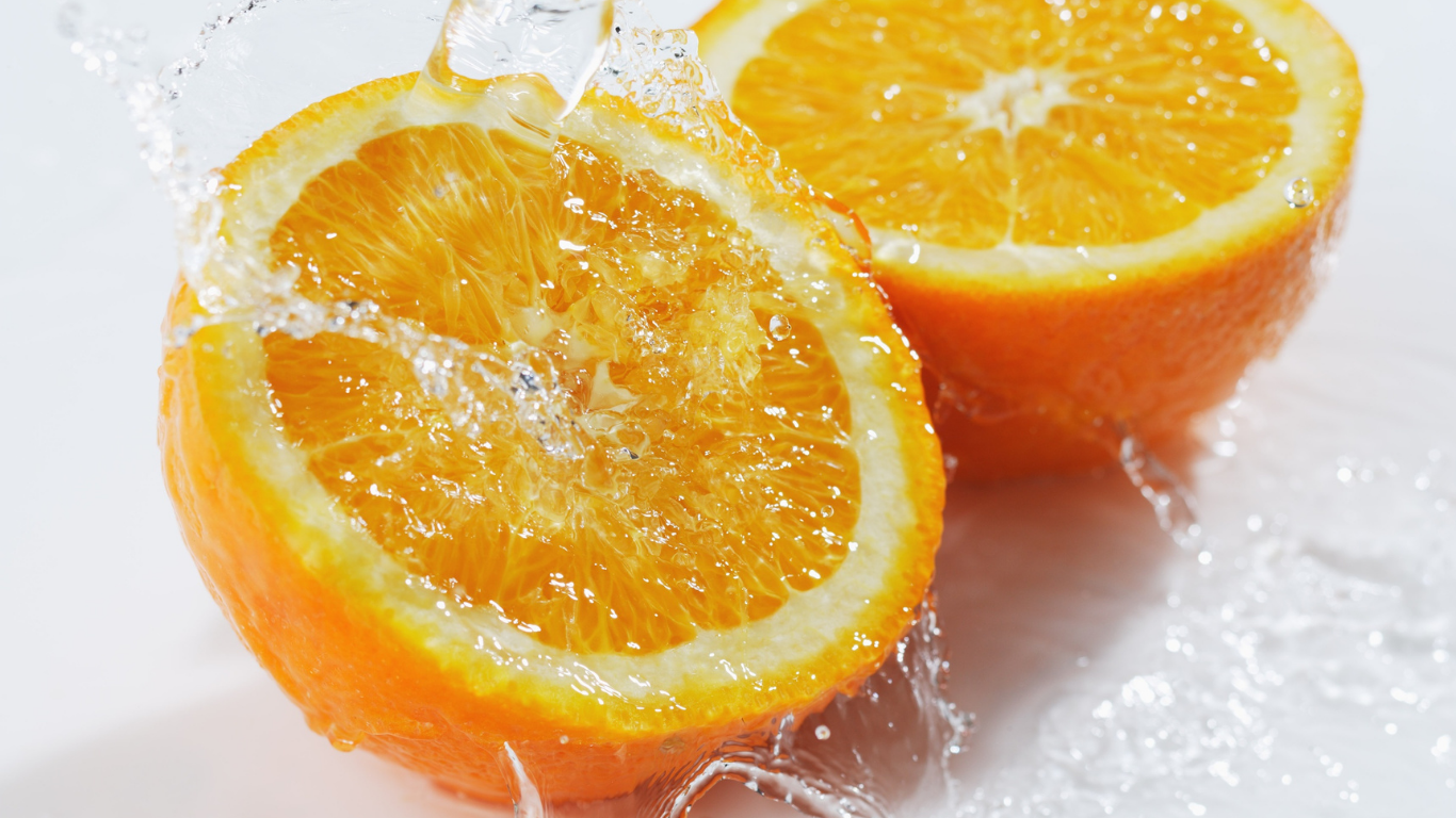 Naranja cortada por la mitad con salpicaduras de agua sobre un fondo blanco.