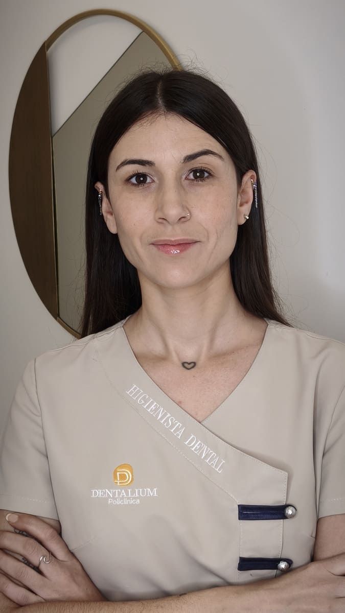 Retrato de una mujer con uniforme beige, de pie con los brazos cruzados frente a un espejo.