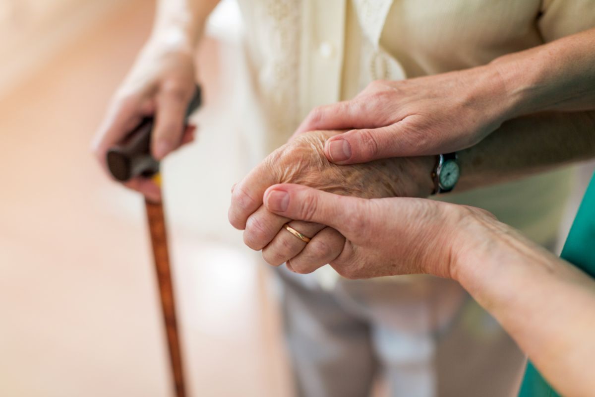 Die Hand einer älteren Dame mit Gehstock wird gehalten
