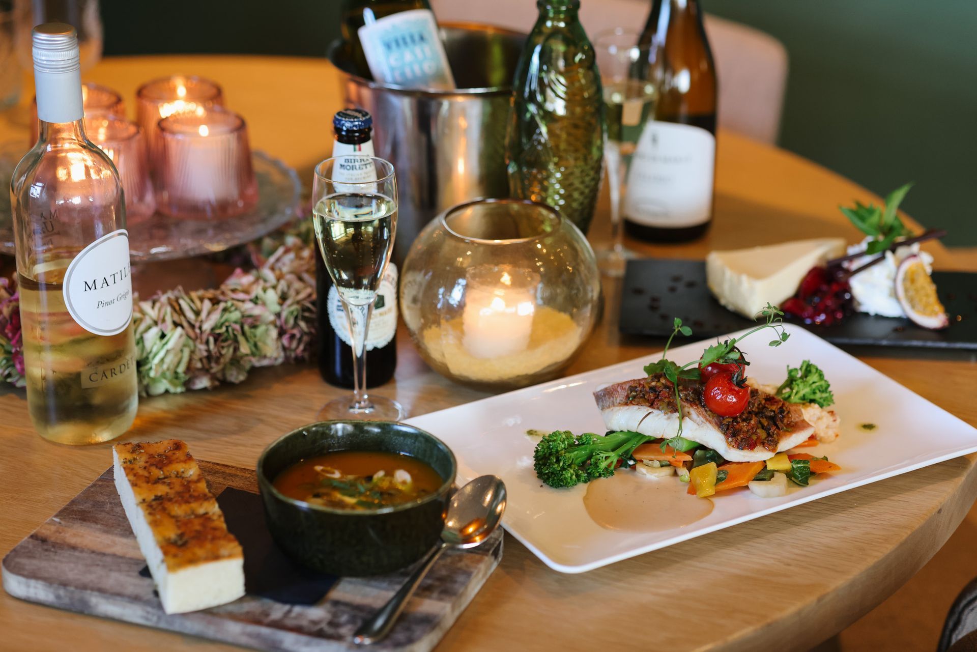 Ein gedeckter Restauranttisch mit Speisen, Weingläsern und einer brennenden Kerze.
