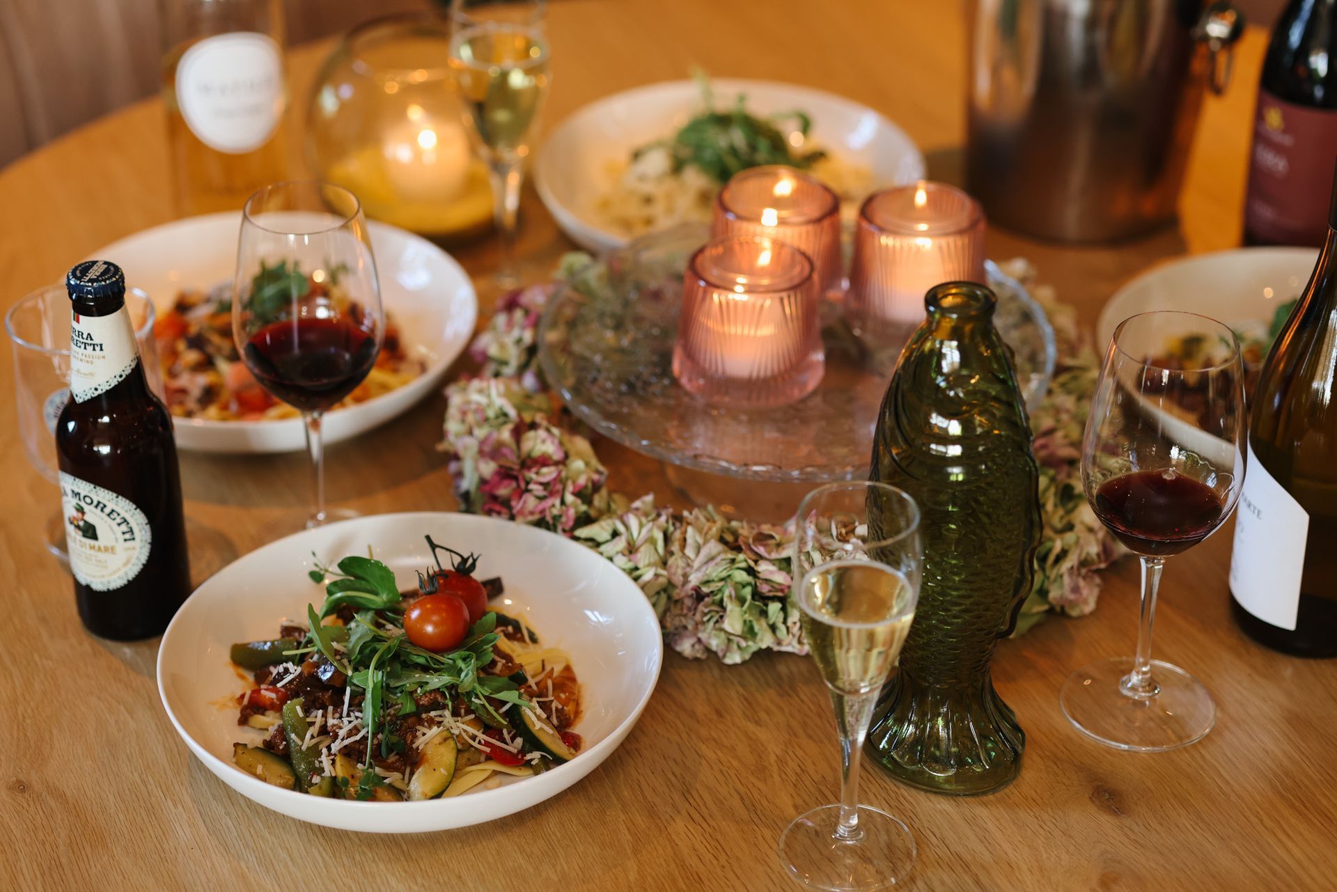 Ein für eine Mahlzeit gedeckter Tisch mit Pastagerichten, Wein, Bier und Kerzen.
