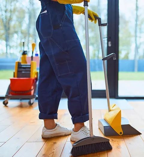 Una persona está parada sobre un piso de madera con una escoba y un trapeador.