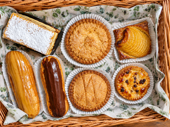 Assortiment de viennoiseries dans des caissettes en papier et gâteau saupoudré de sucre glace dans un plateau tapissé d’un panier