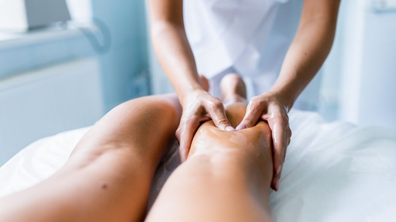 Manos masajeando las piernas de una persona en una camilla de spa.