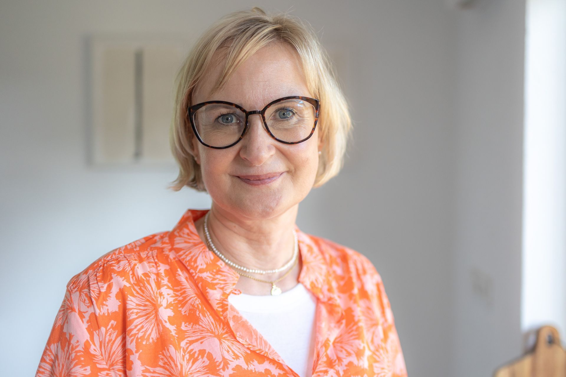 Eine Frau mit Brille und orangefarbenem Hemd lächelt in die Kamera.