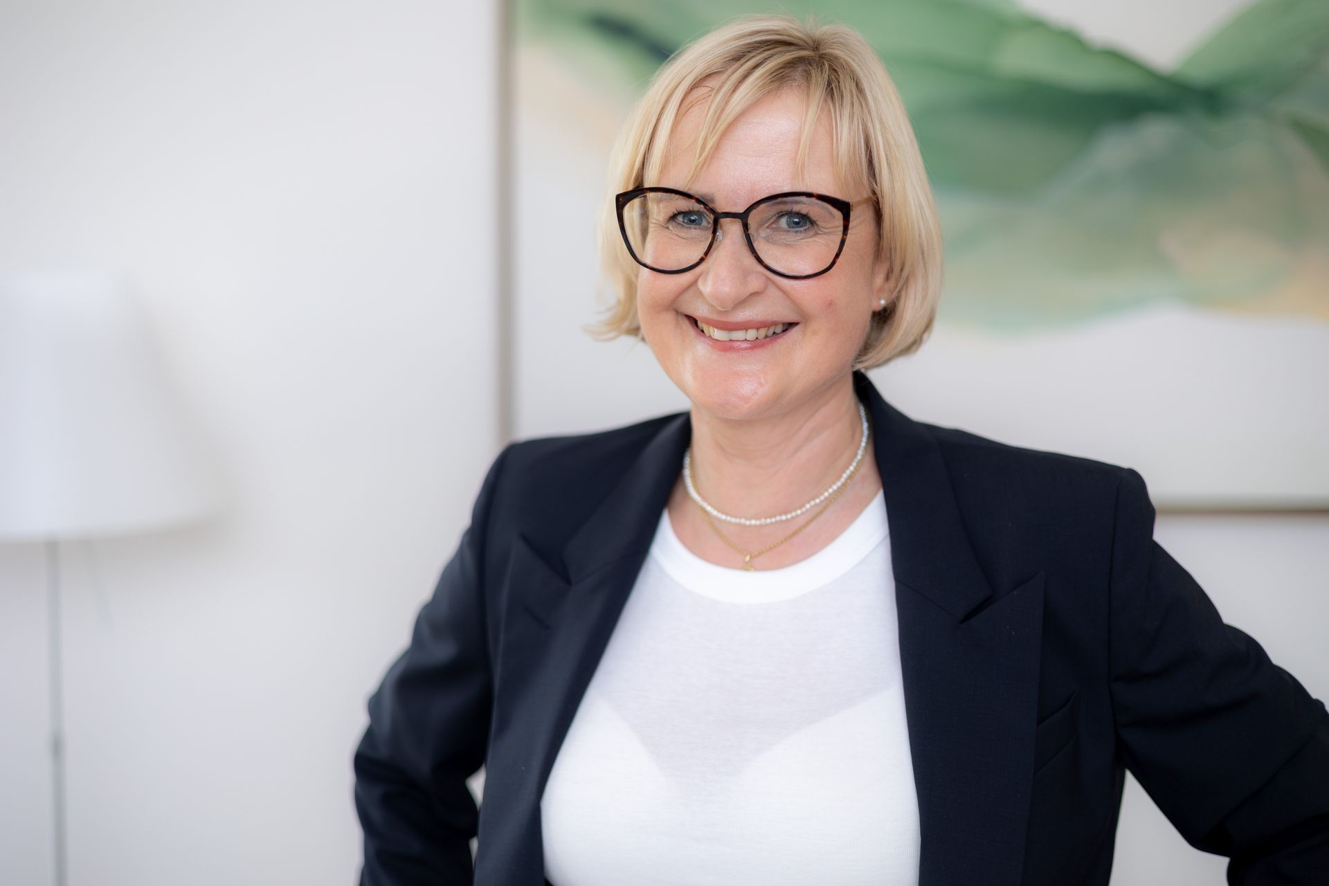 Eine Frau mit Brille und schwarzer Jacke lächelt in die Kamera.