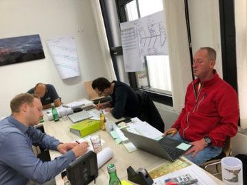 Eine Gruppe Männer sitzt mit Laptops um einen Tisch.