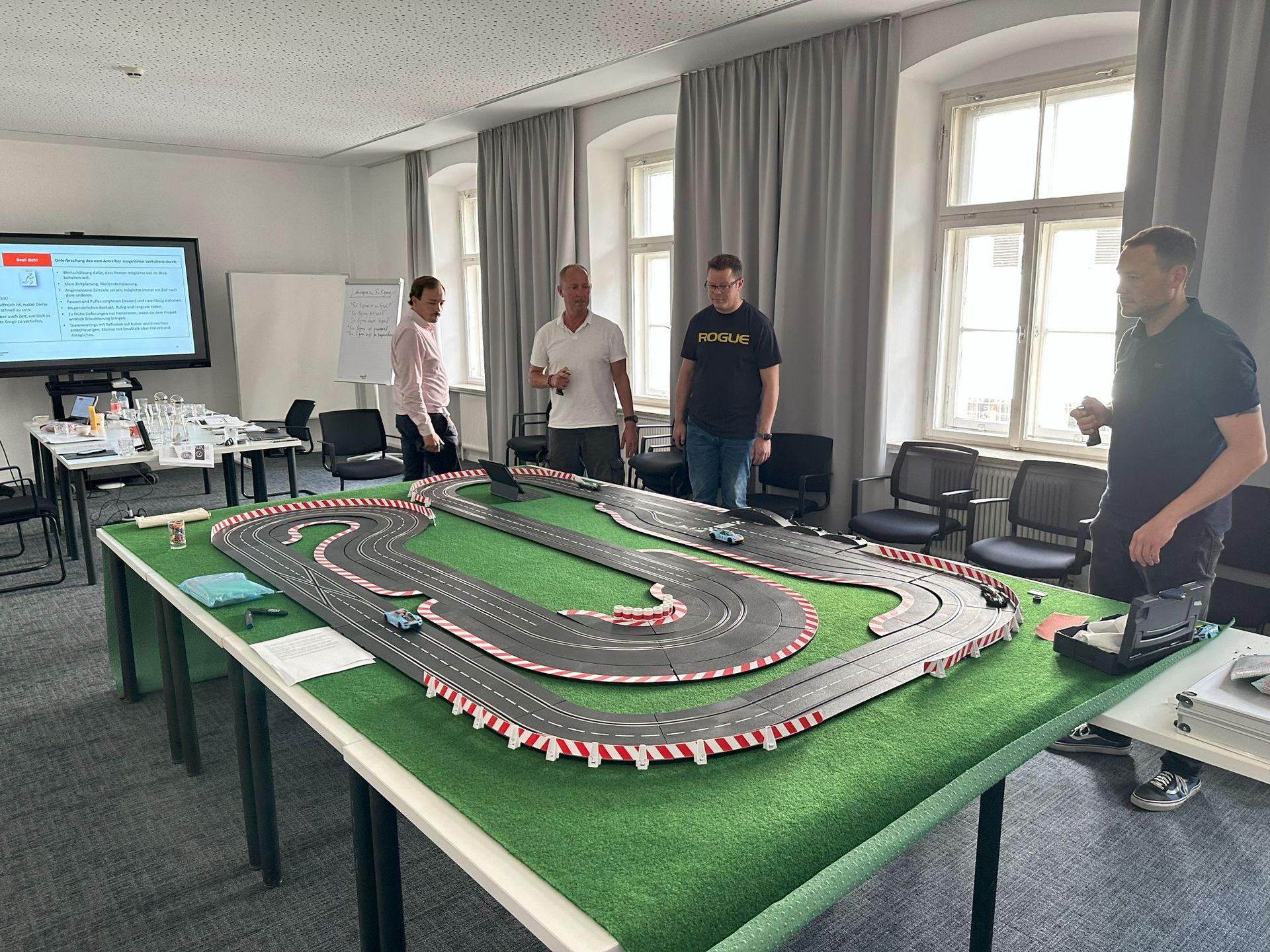 Eine Gruppe von Männern steht um einen Tisch herum , auf dem eine Spielzeug - Rennstrecke steht.