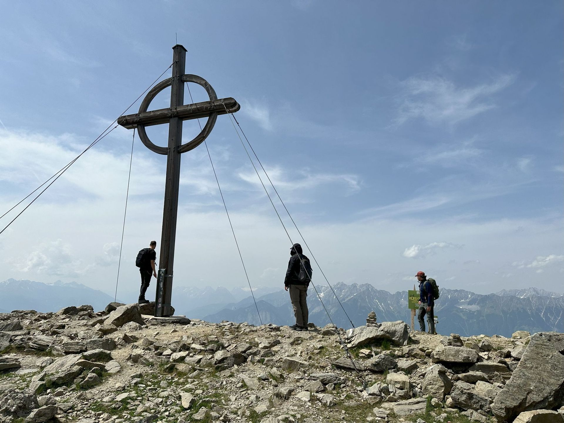 Drei Menschen stehen unter einem Kreuz auf einem Berggipfel.