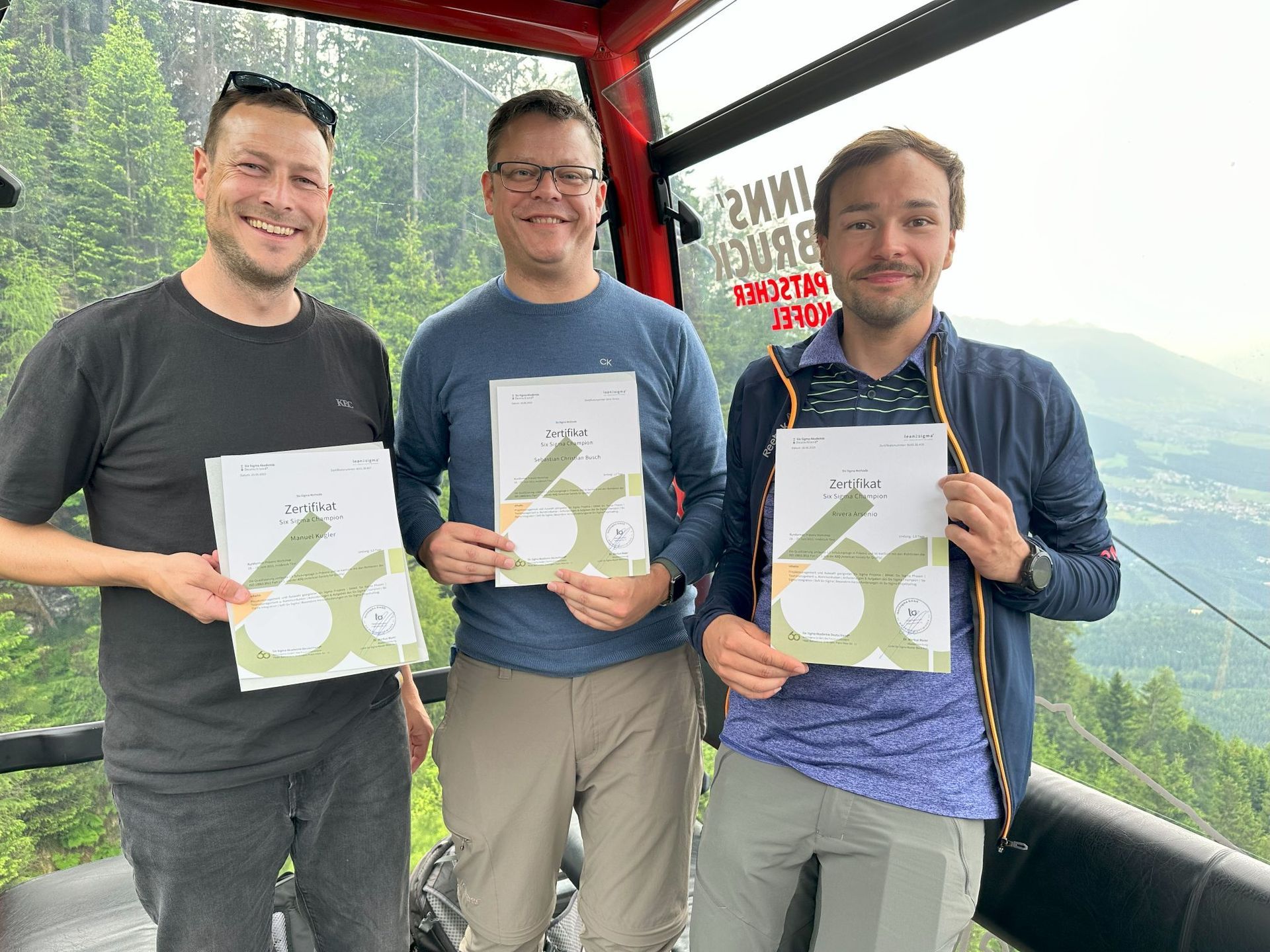 Drei Männer stehen in einer Seilbahn und halten Papiere in den Händen.