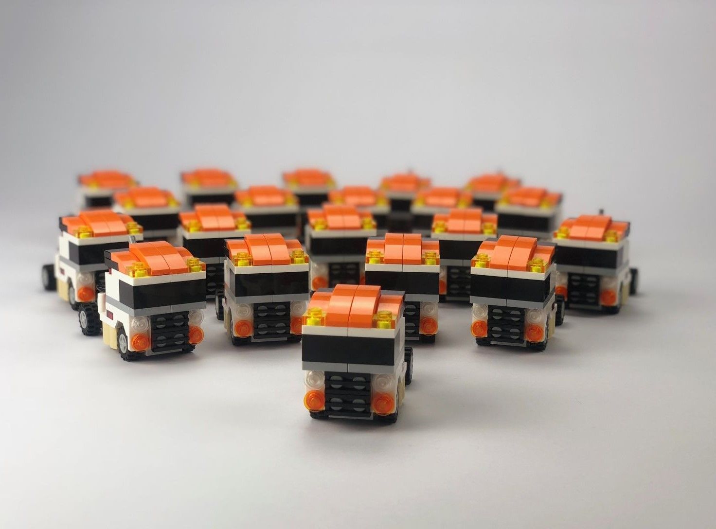 Kleine Lego-Trucks, weiß und schwarz mit orangefarbenen Dächern, gruppiert auf einer weißen Fläche.