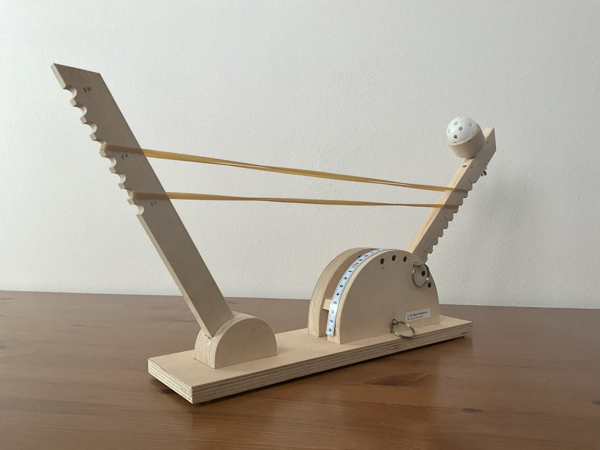 Eine kleine hölzerne Katapult mit einer weißen Kugel, bereit zum Abschuss.