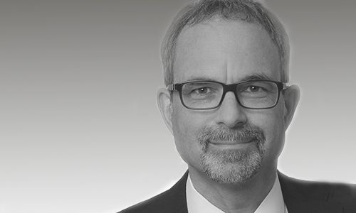 Ein Mann mit Brille und Bart trägt Anzug und Krawatte.