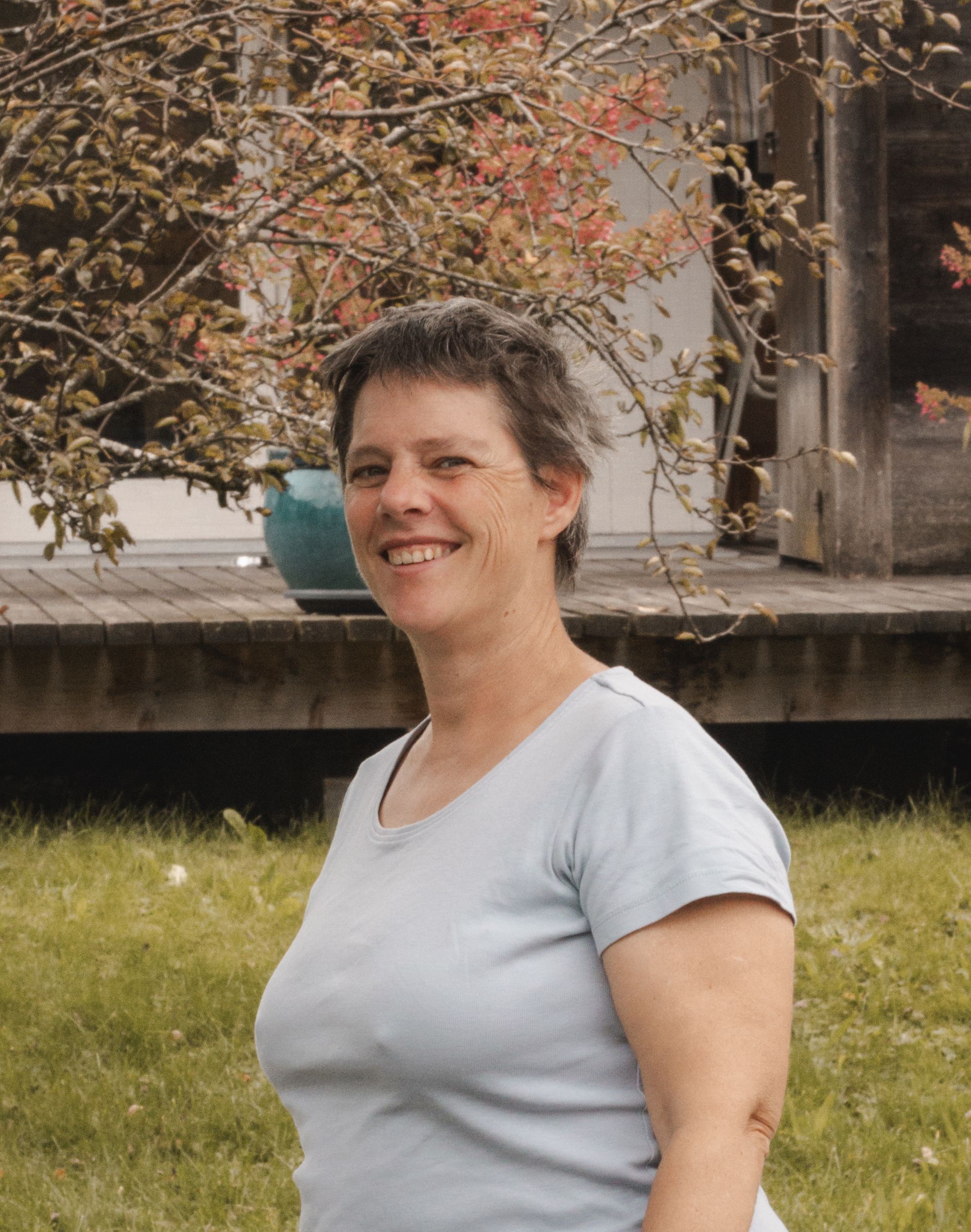 Eine Frau in einem blauen Pullover steht vor einer Holzwand.