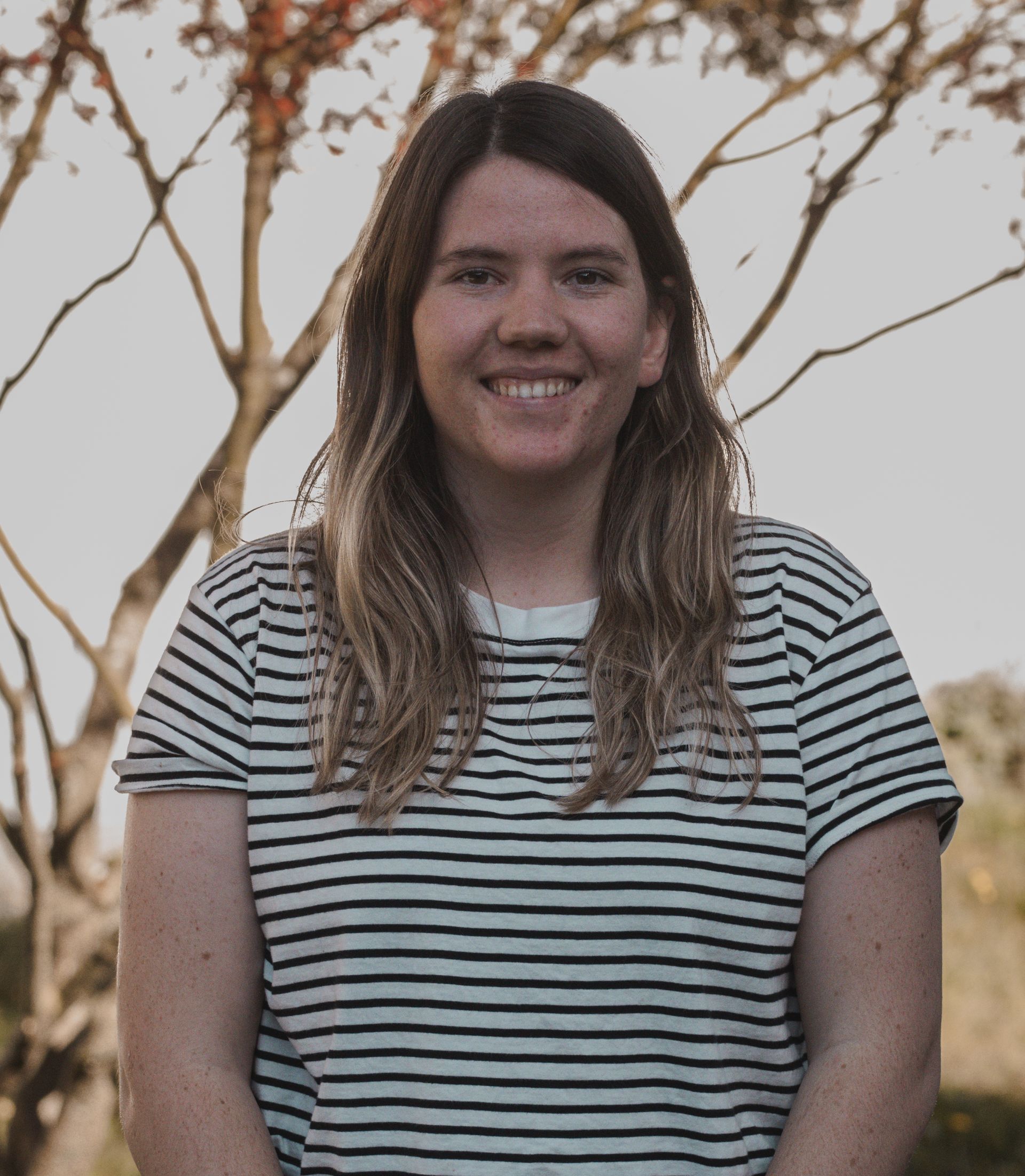 Eine Frau mit Brille und schwarzem Hemd steht vor einer Holzwand.
