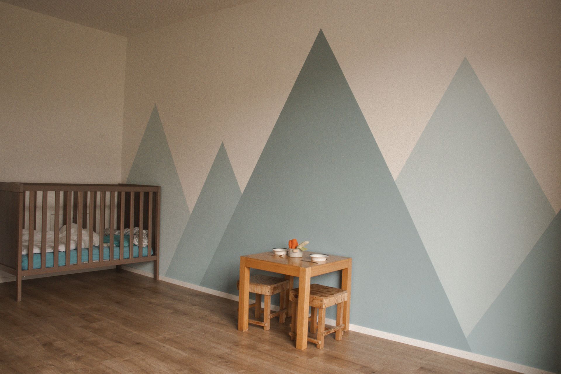 Im Zimmer stehen ein Kinderbett und ein Tisch, an die Wand sind Berge gemalt.