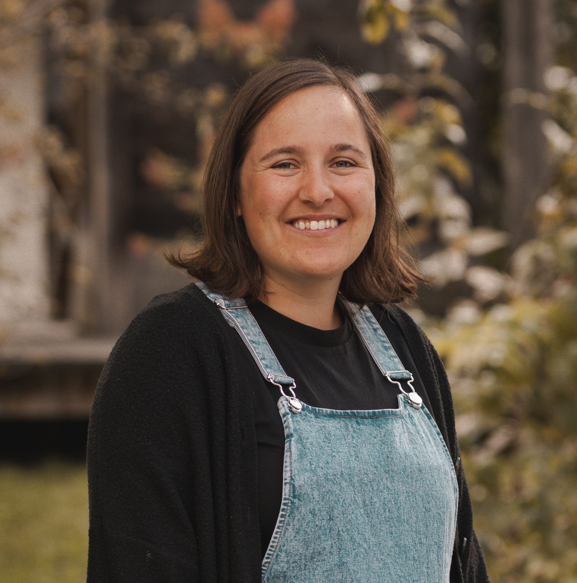 Eine Frau in einem gelben Oberteil lächelt vor einer Holzwand.