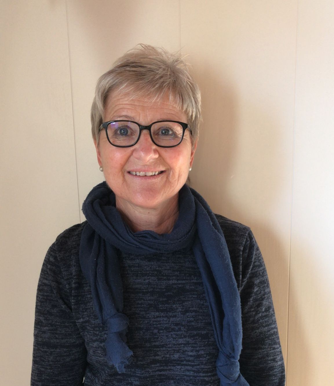 Eine Frau mit Brille und Kopftuch lächelt in die Kamera.