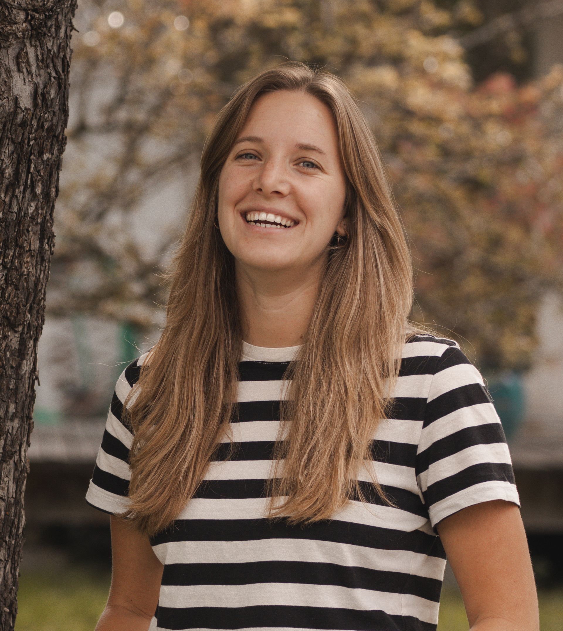 Eine Frau in einem schwarzen T-Shirt steht vor einer Holzwand.