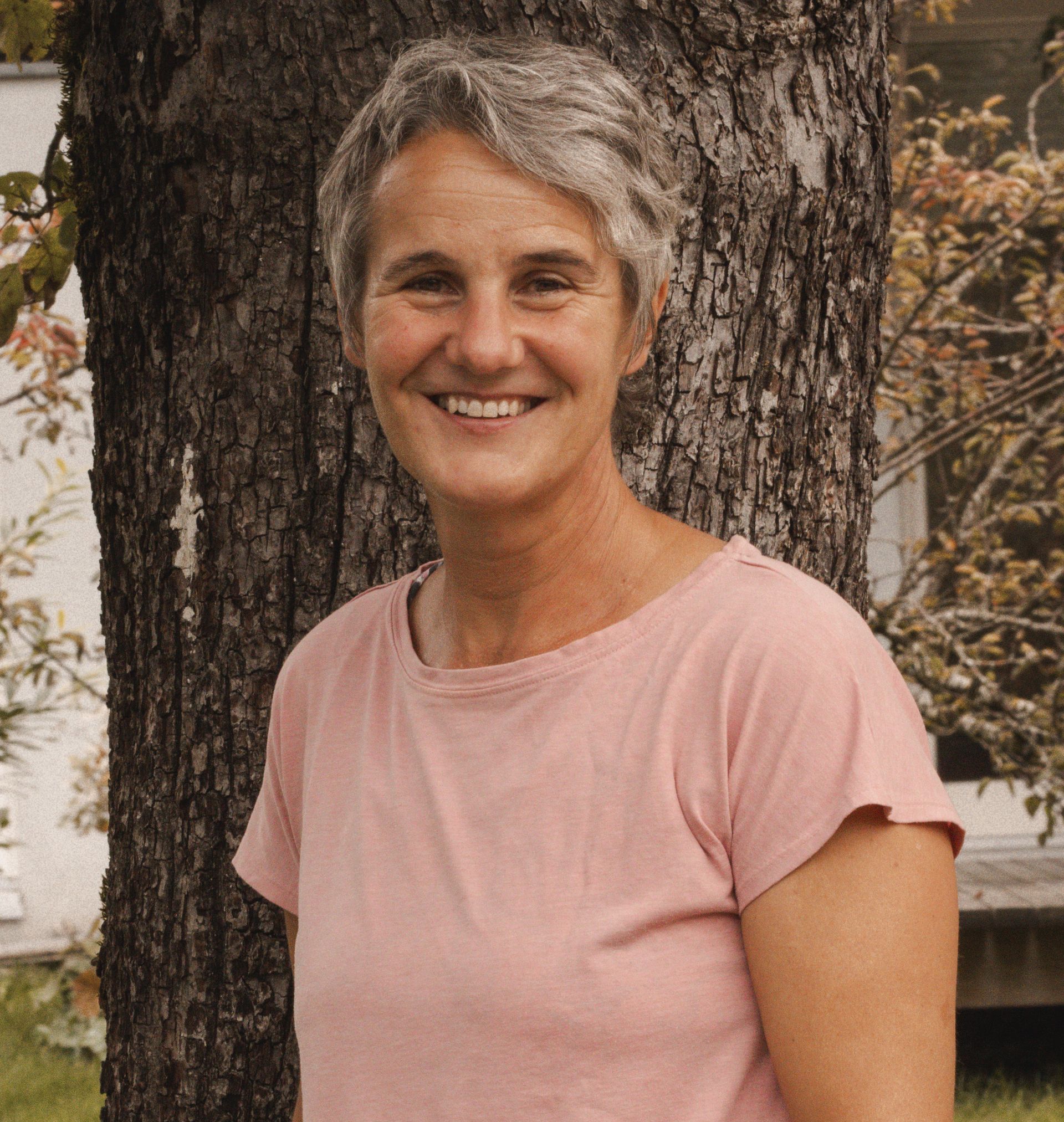 Eine Frau in einem roten Kapuzenpullover steht vor einer Holzwand.