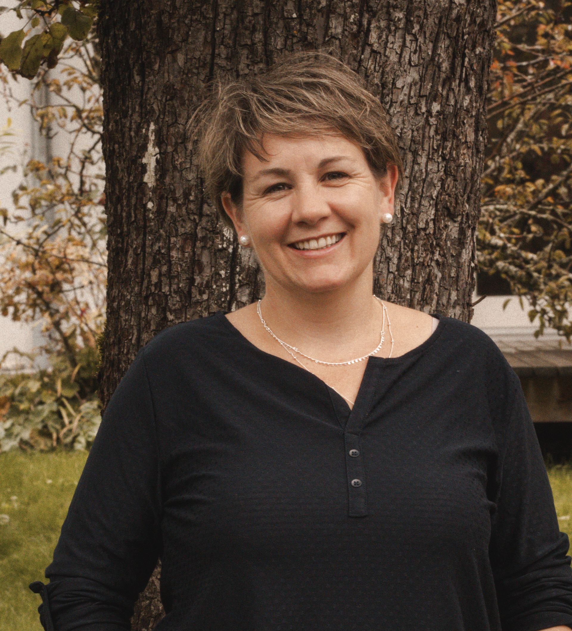 Eine Frau in einem grünen Hemd und blauen Jeans steht vor einer Holzwand.