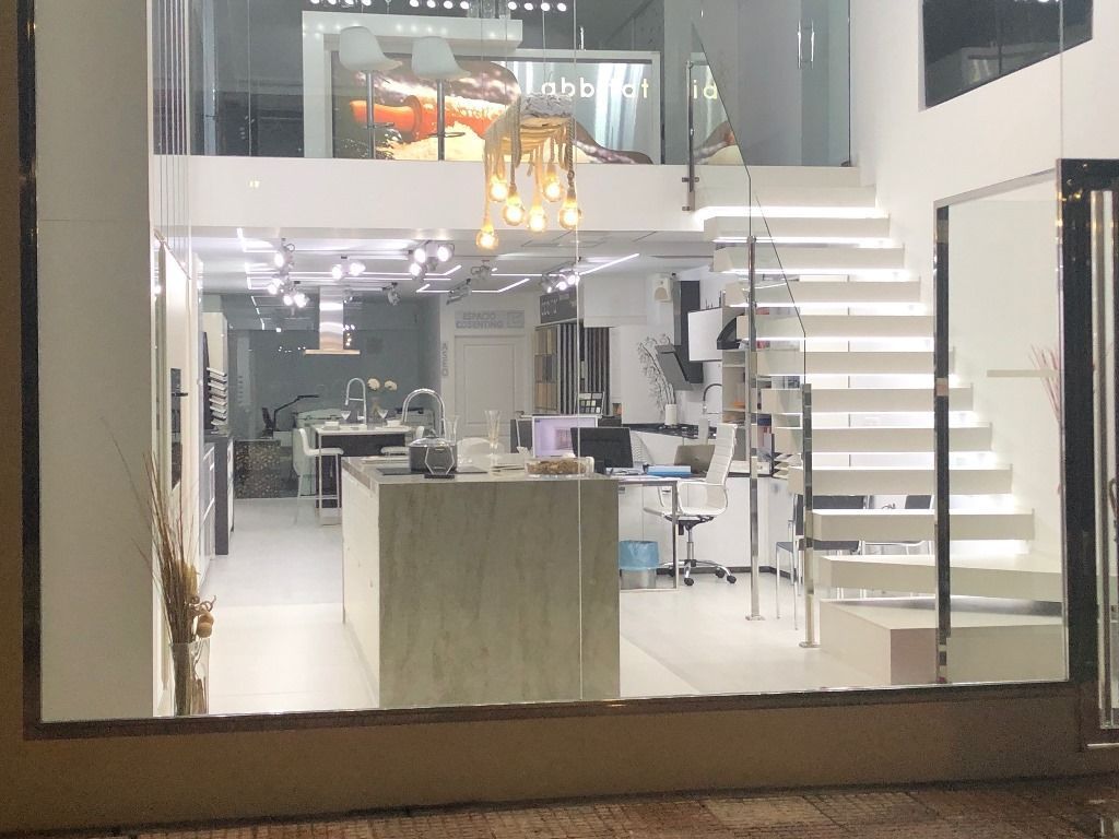 Interior de una sala de exposición moderna con paredes blancas, una escalera y exhibiciones de accesorios de cocina y hogar.