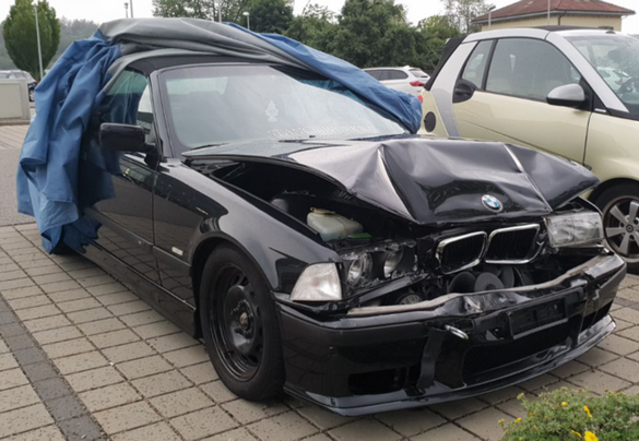 Ein schwarzes Auto mit kaputter Motorhaube ist mit einer blauen Plane abgedeckt.