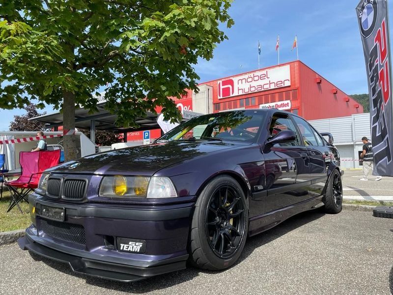 Ein lila BMW M3 parkt vor einem roten Gebäude.