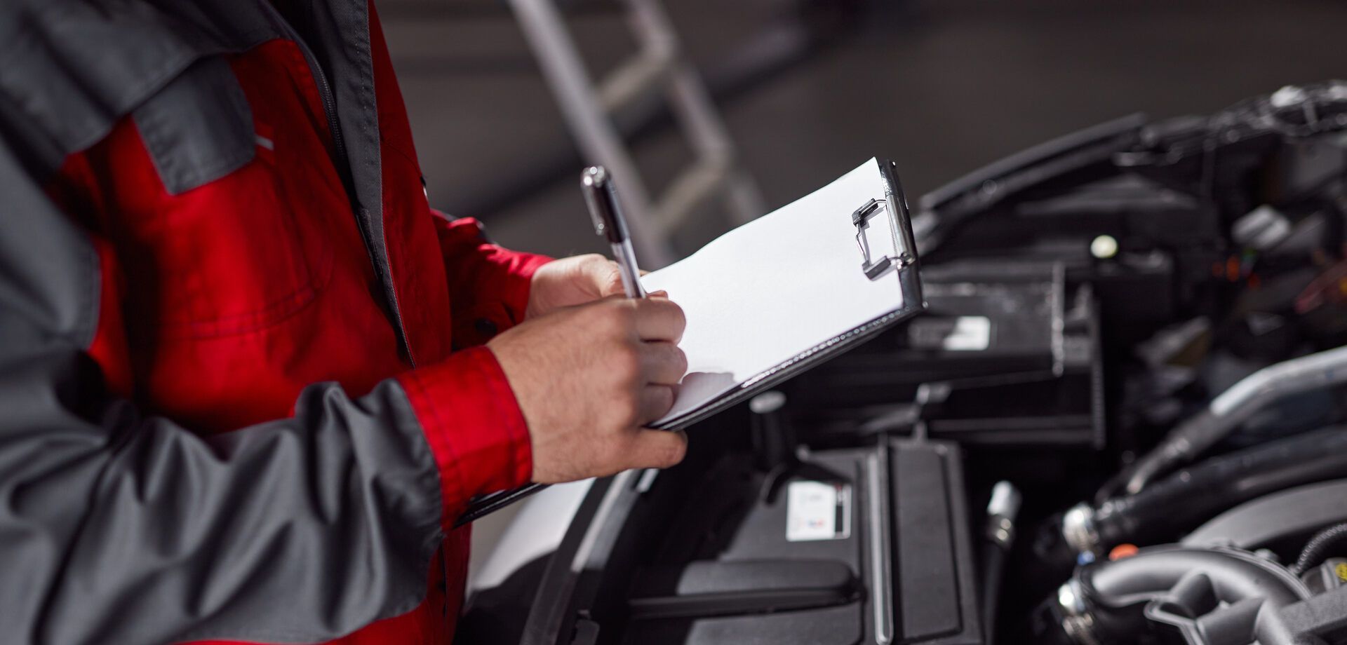 Ein Mechaniker schreibt auf einem Klemmbrett, während er an einem Auto arbeitet.