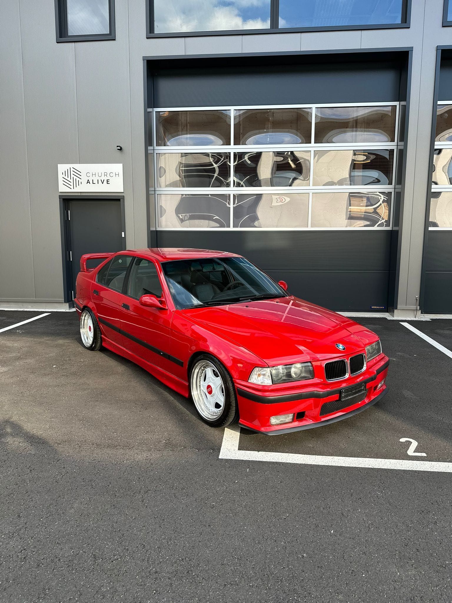 Ein roter BMW steht auf einem Parkplatz vor einem Gebäude.