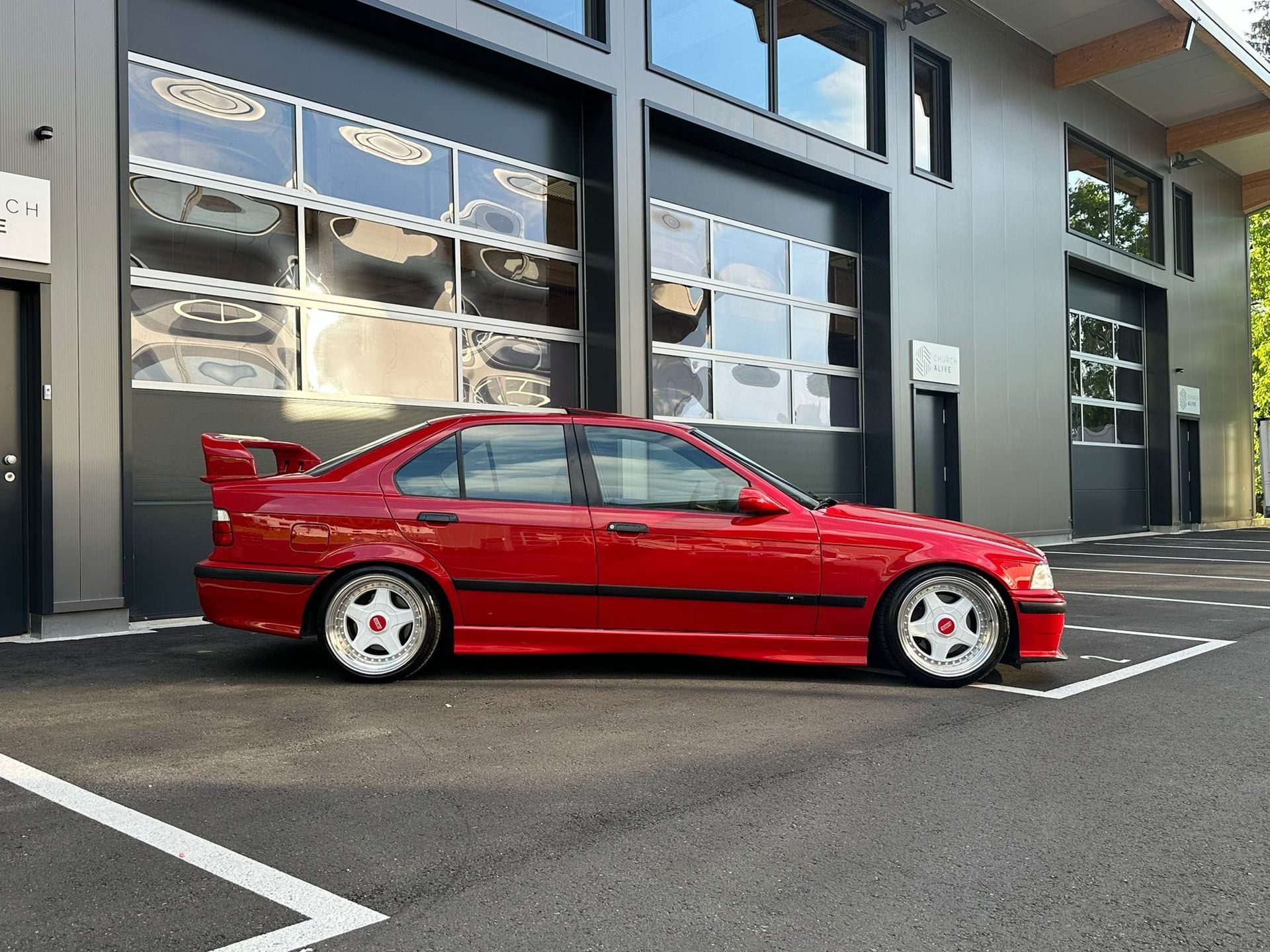 Ein rotes Auto steht auf einem Parkplatz vor einem Gebäude.