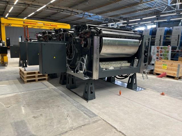 Una gran máquina está en un almacén al lado de una grúa amarilla.