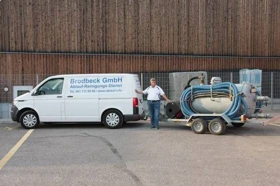 Mann neben weissem Lieferwagen mit blauem Schlauchhaspelanhänger auf einem Industriegelände