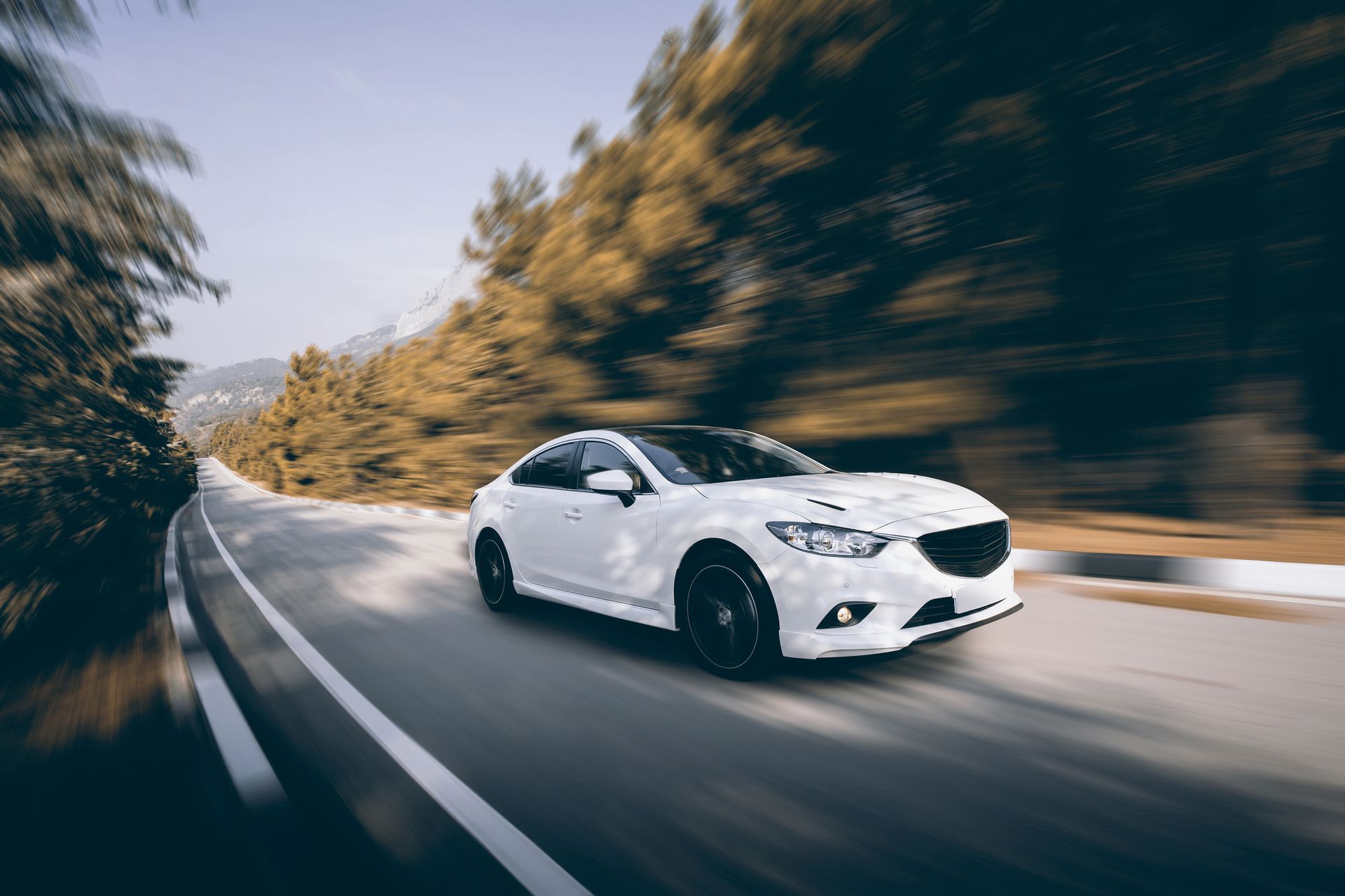 Voiture blanche roulant à vive allure sur une route sinueuse à travers une forêt ; effet de flou de mouvement.