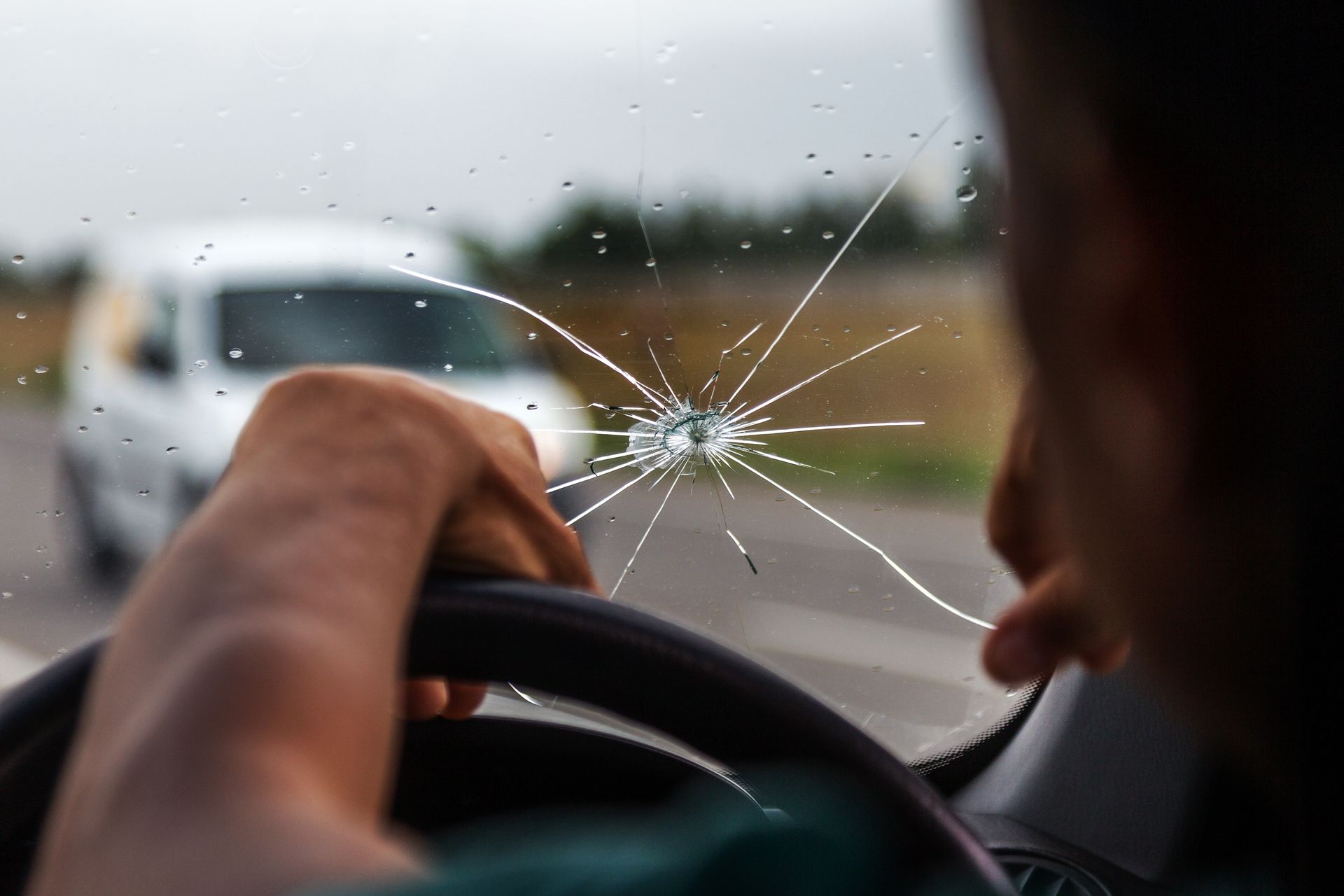 Une personne conduisant une voiture avec un pare-brise fissuré s'approche d'un autre véhicule sur la route.
